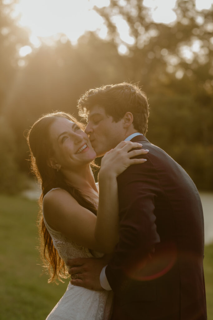 The groom kissing his bride on the cheek during golden hour portraits