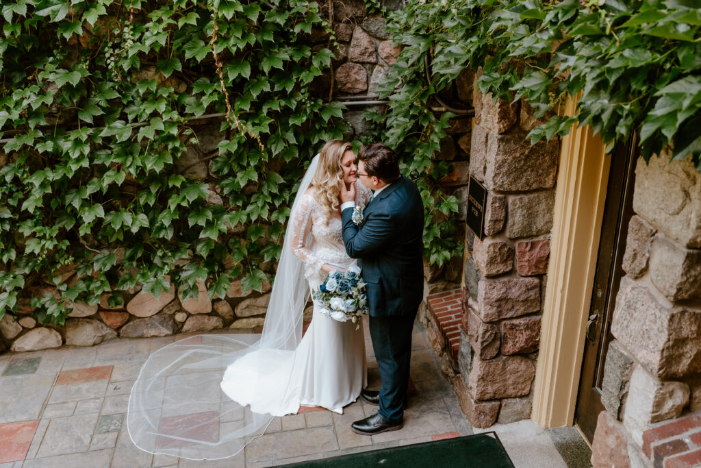 A bride and groom look lovingly at each other amongst a brick wall of ivy.